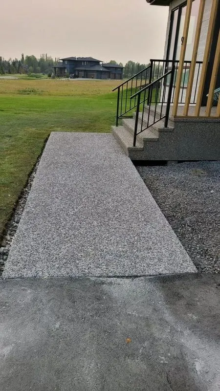 Exposed aggregate concrete walkway leading to stairs with a black railing