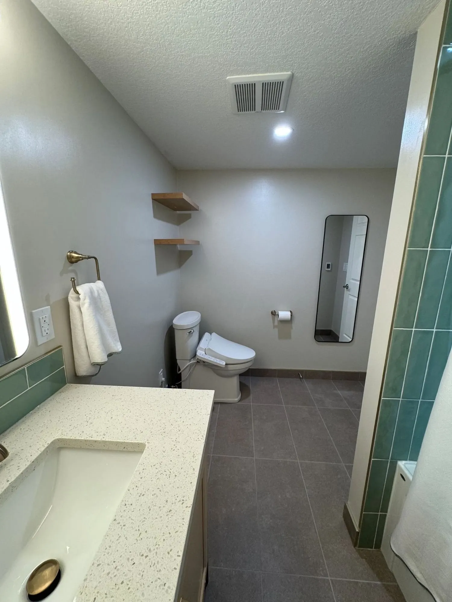 Bathroom with sage green stacked tile in a walk-in shower, a quartz vanity top and brushed brass fixtures