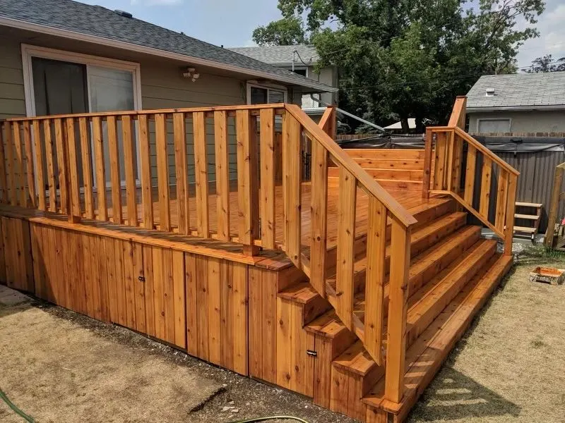 Raised cedar deck with a railing and wide stairs beside a house
