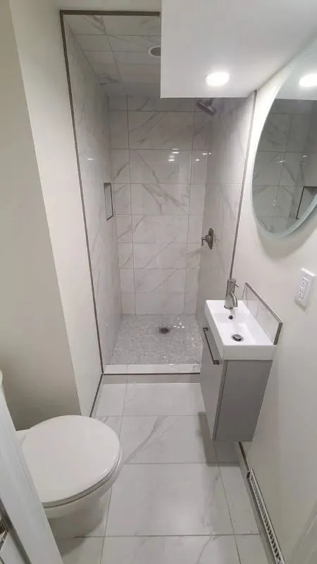 Small bathroom with a white marble-look tiled walk-in shower, glass panel, round mirror and wall-hung vanity