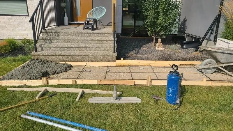 Wood forms and gravel base set out for a new concrete walkway beside a lawn