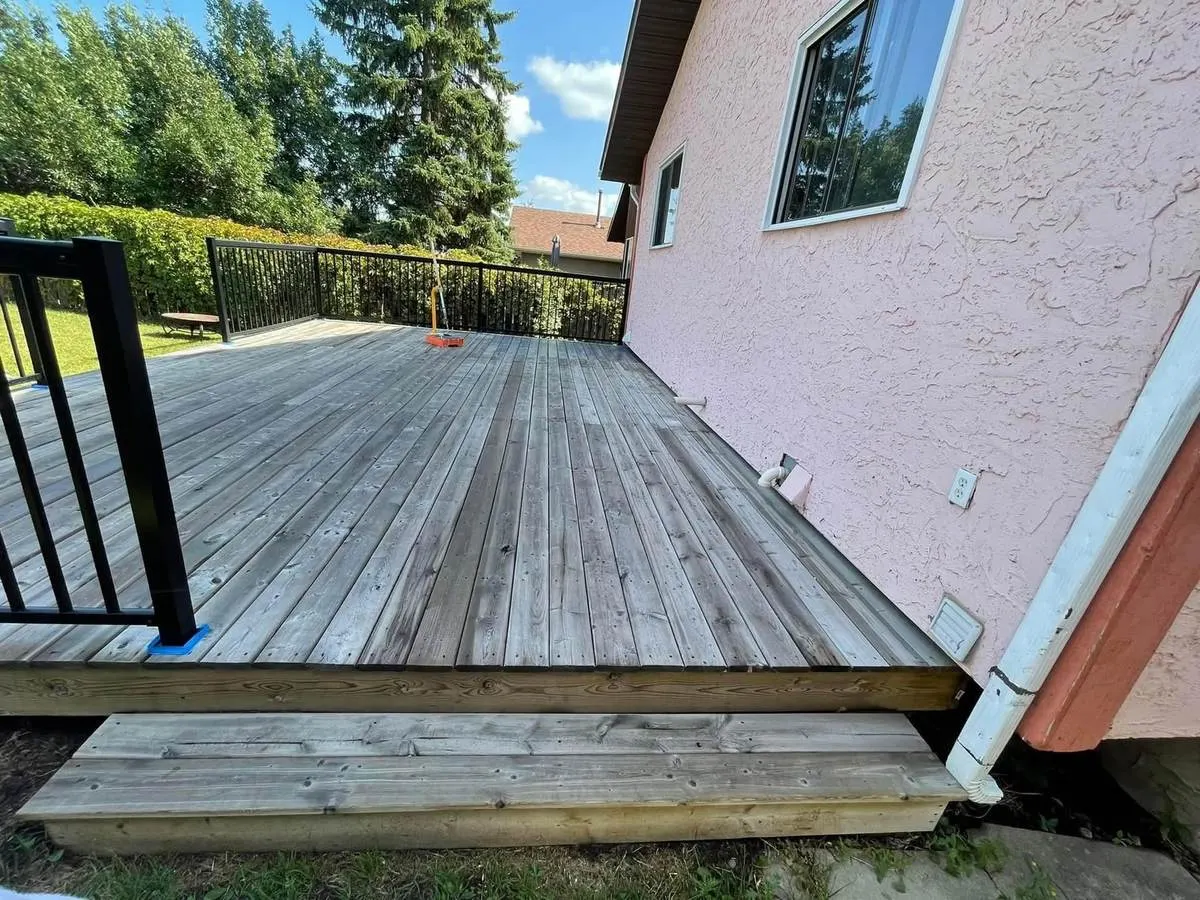 Weathered grey cedar deck boards with black aluminum railing before staining