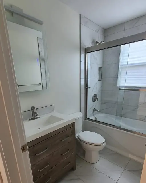 Bathroom with a wood-grain vanity, white marble-look tile and a glass sliding door on the tub and shower