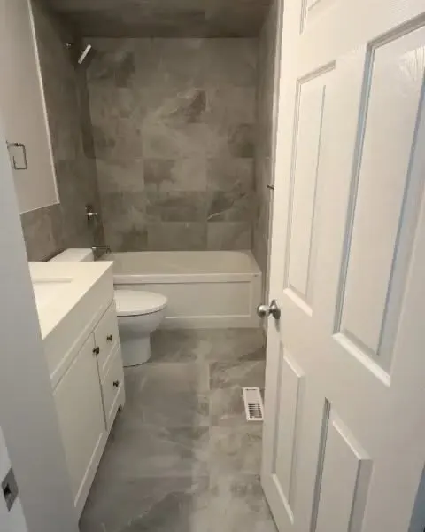 Bathroom with grey stone-look tile on the tub surround and floor, a white vanity and a white tub