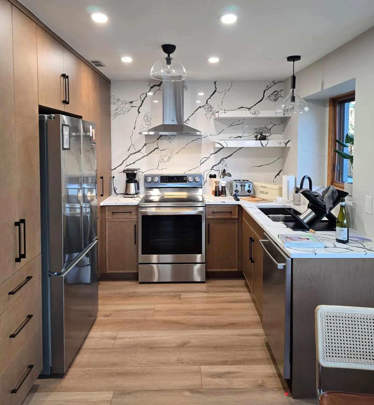 Renovated kitchen with wood-tone cabinetry, a veined stone-look backsplash, range hood and stainless appliances