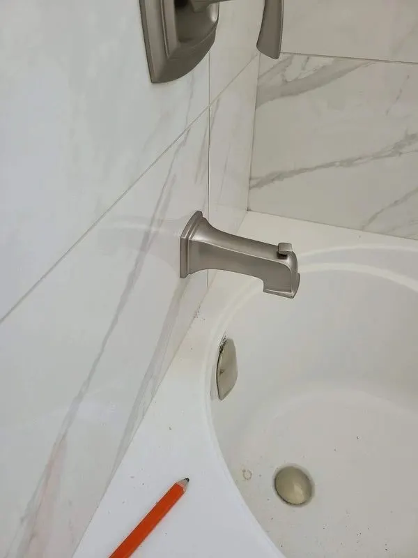 Close view of a white bathtub with a satin nickel tub spout against large marble-look wall tile