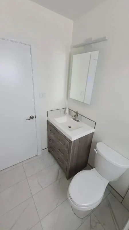 Small powder room with a wood-grain floating vanity, mirror cabinet and toilet on light tile